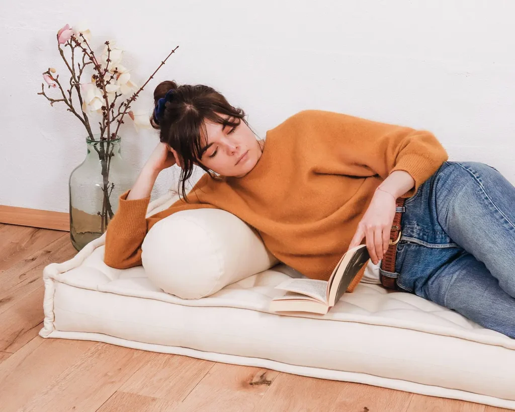femme allongée sur un matelas en laine et un coussin cylindrique