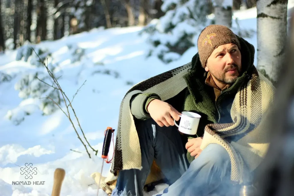 man täckt med en ullfilt som dricker te i snön 