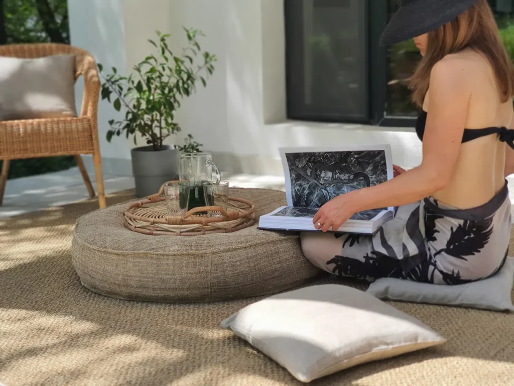 vrouw zittend op een plat geweven wollen tapijt, een boek lezend naast een sierkussen en een ronde tafel