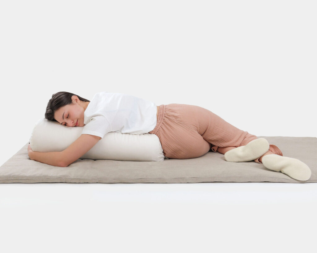 woman resting on a wool yoga mat while hugging a wool yoga bolster