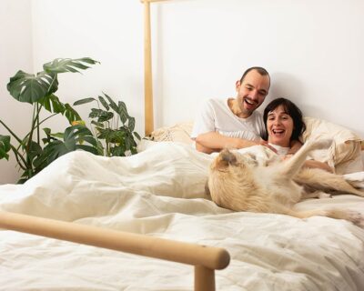 Paar im Bett mit Hund, zugedeckt mit Couples' Wollbettdecke