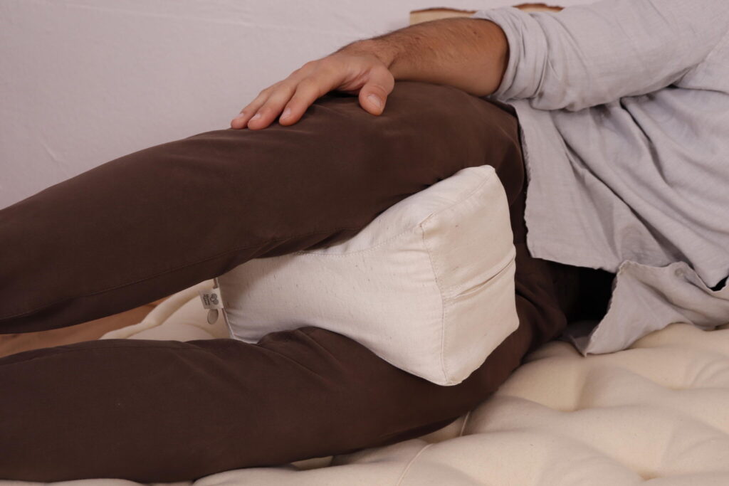 man som vilar på en madrass av ull med en knäkudde mellan benen