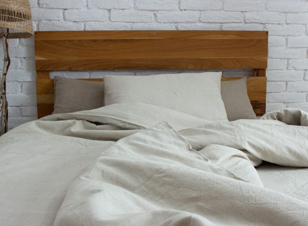 linnekuddar och sängkläder mot trähuvudgavel och rustik vägg