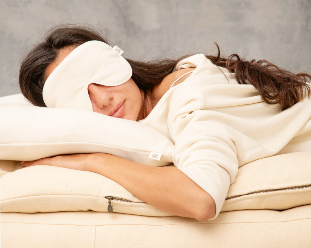 Frau schläft auf einem Wollbett mit einem Wollkissen und einer Schlafmaske aus Wolle