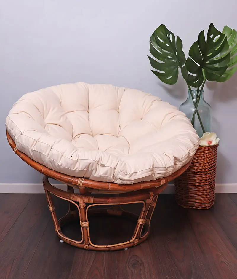 Papasan-stoel met een wollen Papasan-stoelkussen naast een plant in een vaas