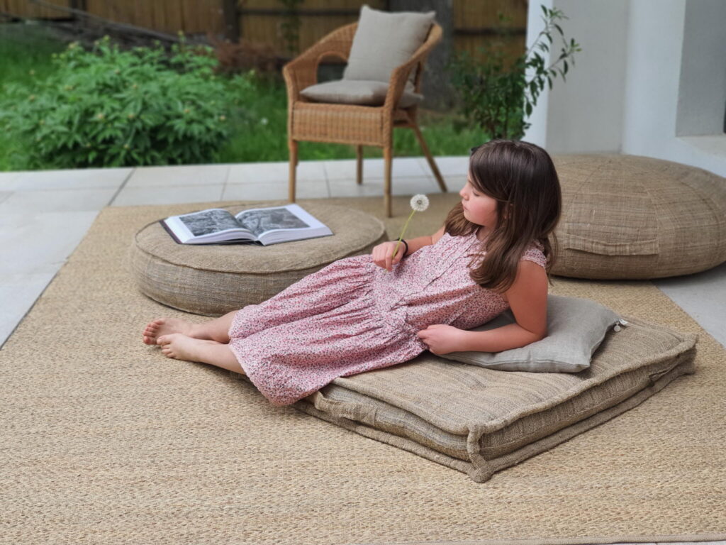 meisje dat ontspant op wollen kussens, met een paardenbloem in haar hand, naast een open boek
