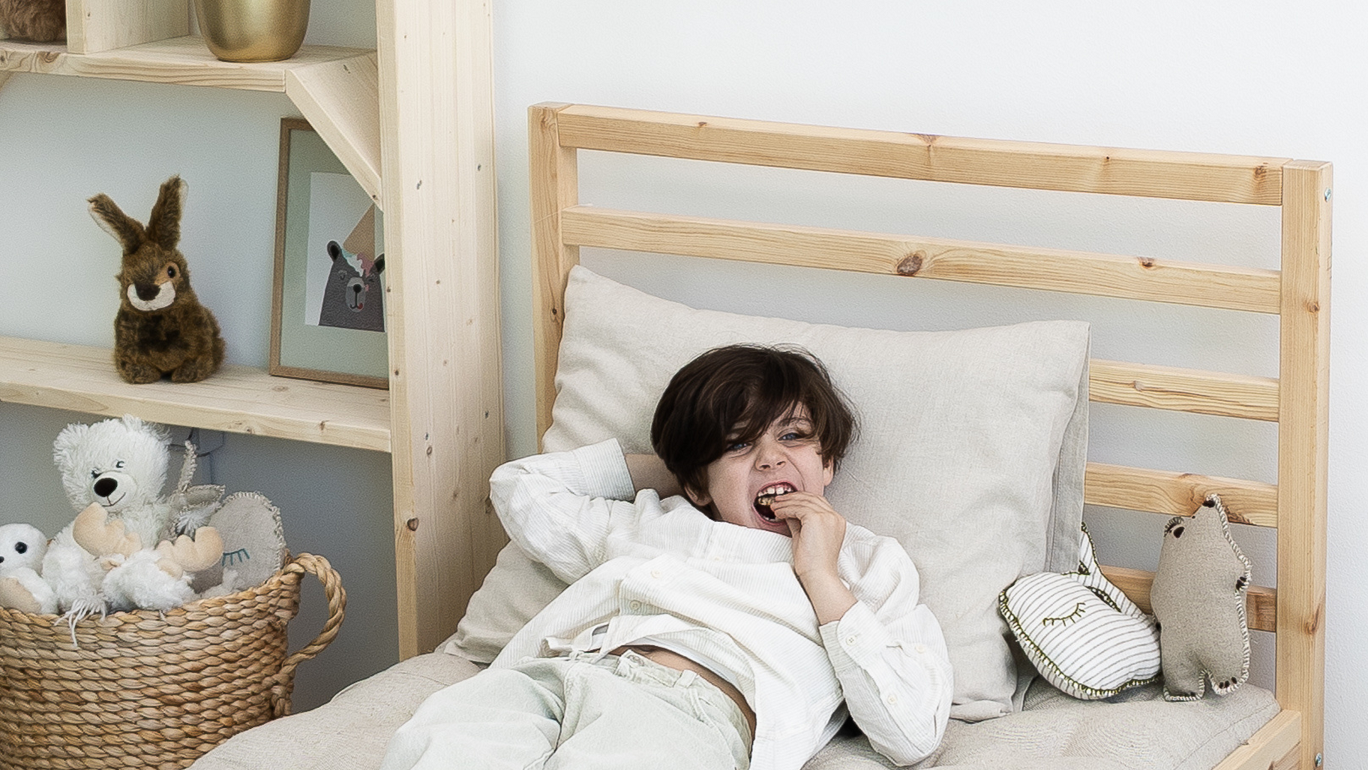kid laying on a home of wool wool bed and a wool pillow with a wooden bed frame while eating a snack in a cozy room setting