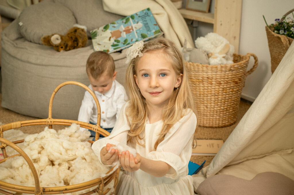 kid holding wool stuffing next to a basket of wool stuffing in a cozy room