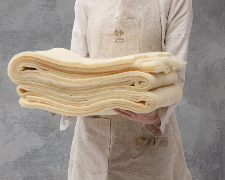 wool batting folded and held by a person with a home of wool apron