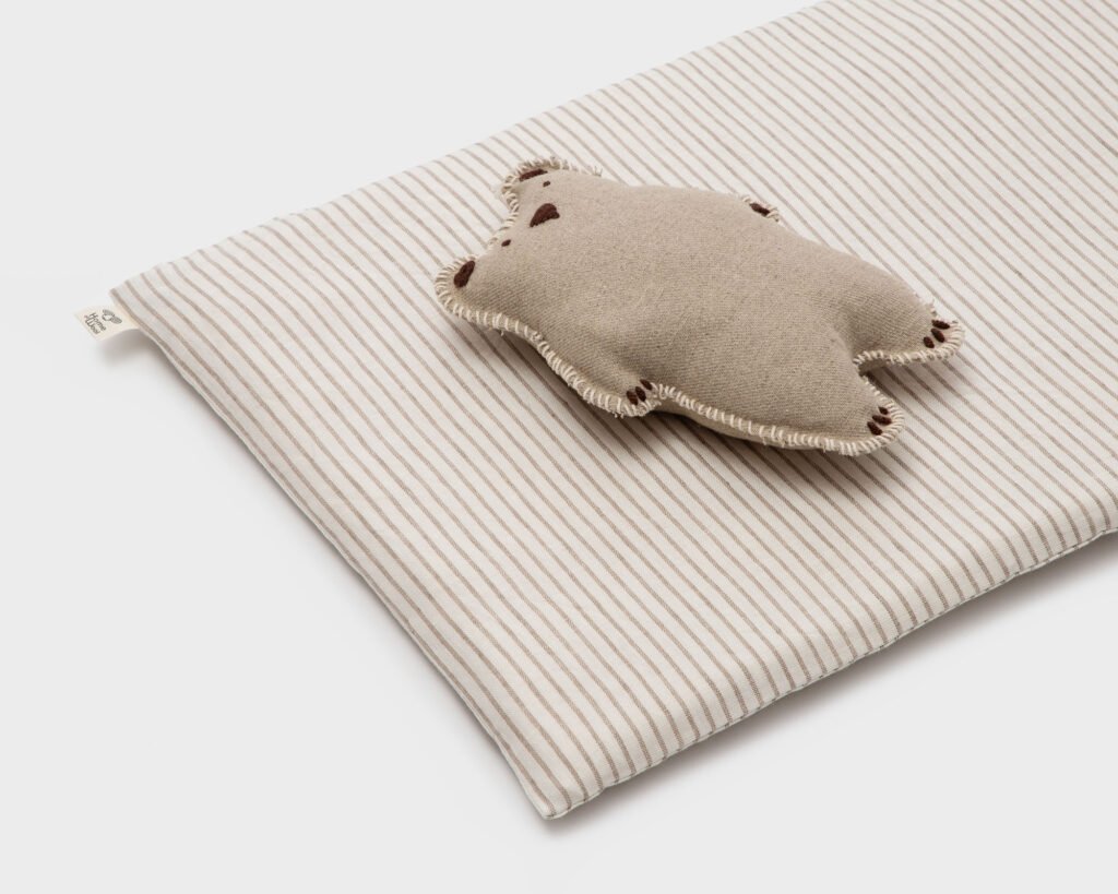 Tapis de jeu rectangulaire en laine pour bébé, à rayures en lin, avec un jouet en laine sur le dessus.