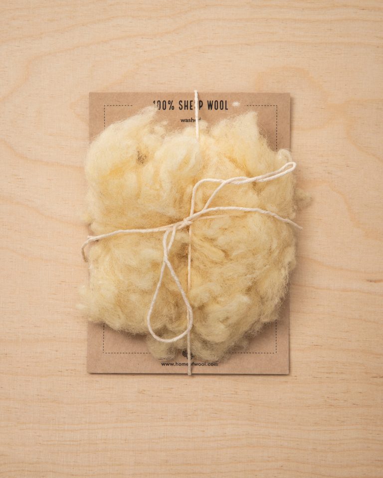 Eine Handvoll Wolle auf einem gebrandmarkten Kartonstück, das mit einer Schnur zusammengebunden ist.